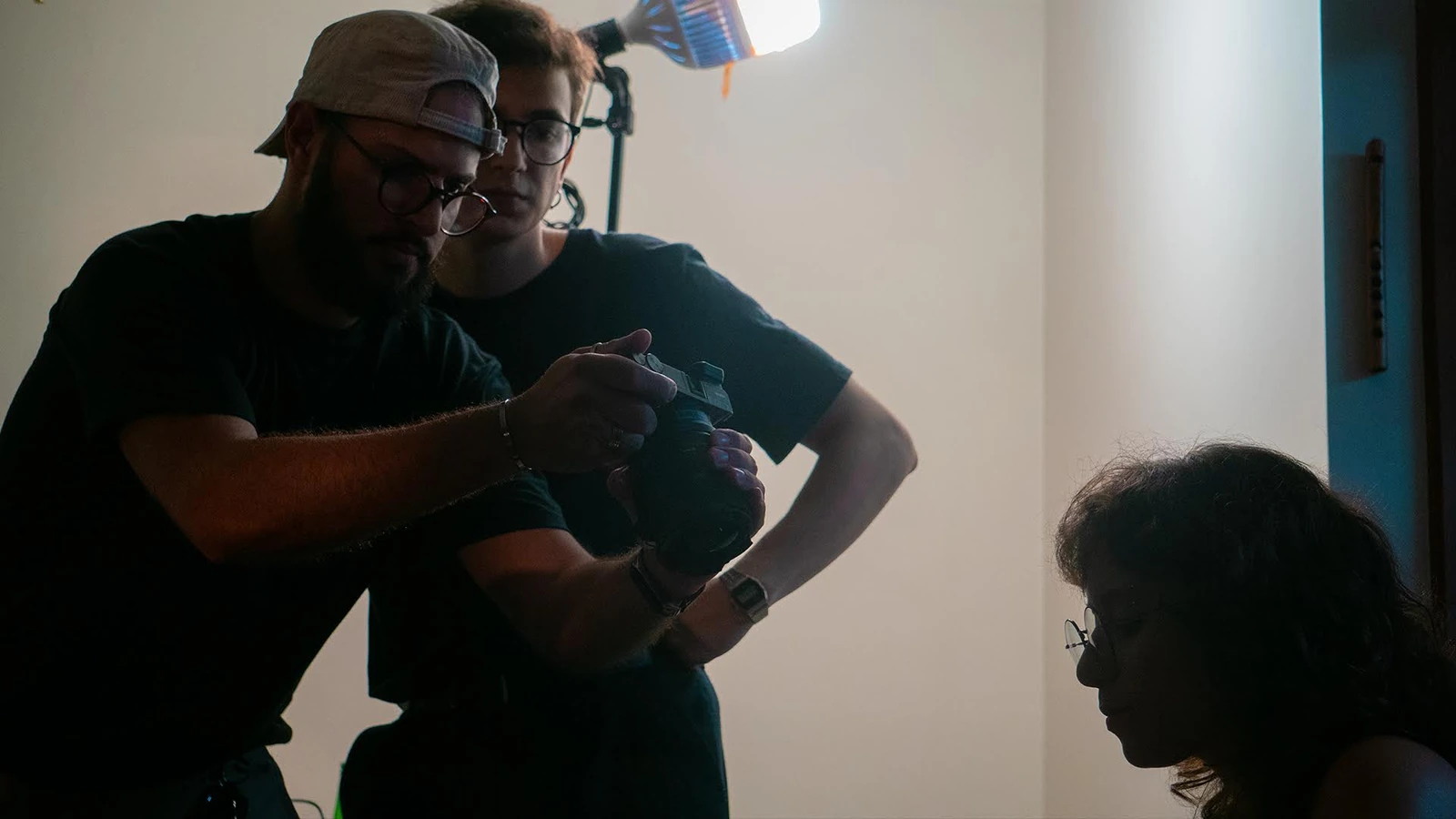 Equipe conferindo a câmera durante a filmagem, com iluminação de set ao fundo.